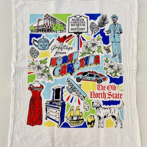 A multicolored cotton tea towel with a printed design featuring historical artifacts and symbols, with text reading 'Greetings from North Carolina, The Old North State'.