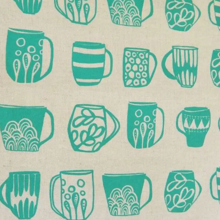A close-up of a fabric or wallpaper pattern featuring teal green stylized coffee mugs printed on a warm beige linen-like background.