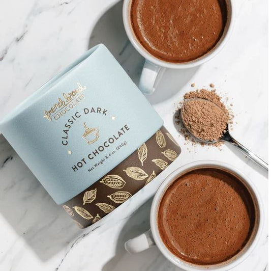 Two cups of hot chocolate with a container of classic dark hot chocolate on a marble surface.