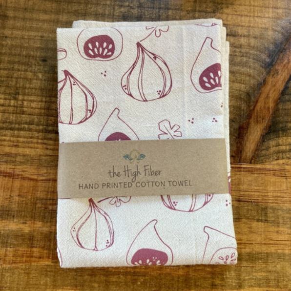 Folded hand-printed cotton towel with fig pattern on a wooden surface, branded 'the High Fiber'.