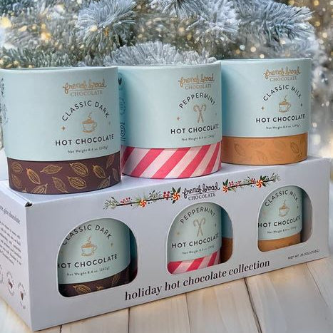 Four containers of hot chocolate in a decorative box with a Christmas tree in the background.
