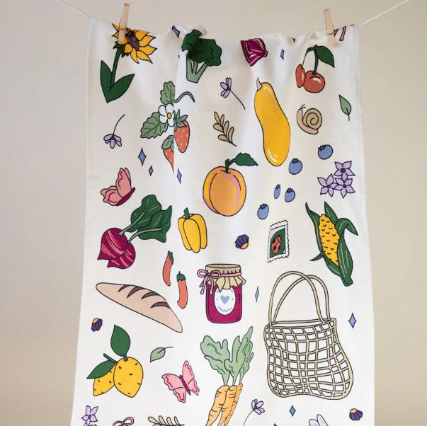 Tea towel with colorful illustrations of fruits, vegetables, and a basket on a white background.