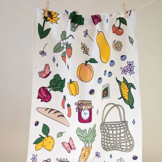 Tea towel with colorful illustrations of fruits, vegetables, and a basket on a white background.