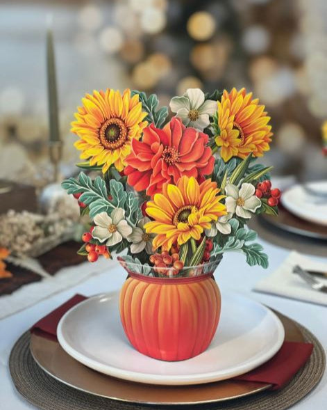 Colorful floral arrangement in a pumpkin-shaped vase on a table setting.