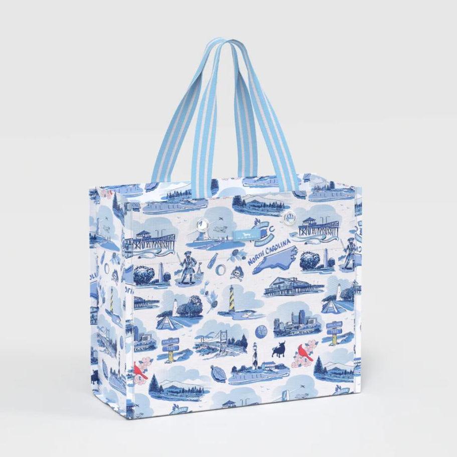 A reusable tote bag with a blue and white coastal illustration pattern, featuring light blue and white striped handles, shown on a light gray background.