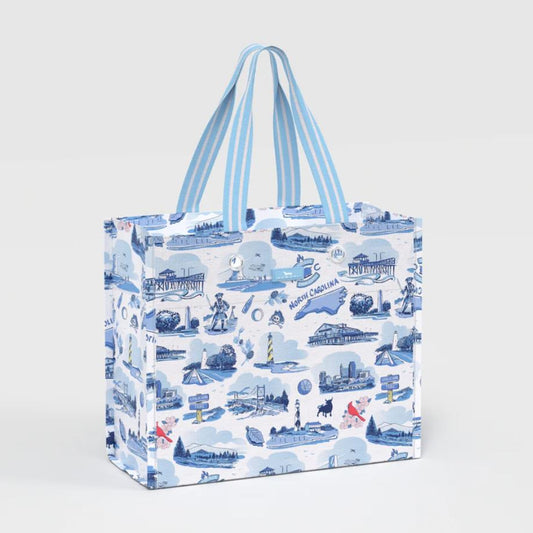 A reusable tote bag with a blue and white coastal illustration pattern, featuring light blue and white striped handles, shown on a light gray background.