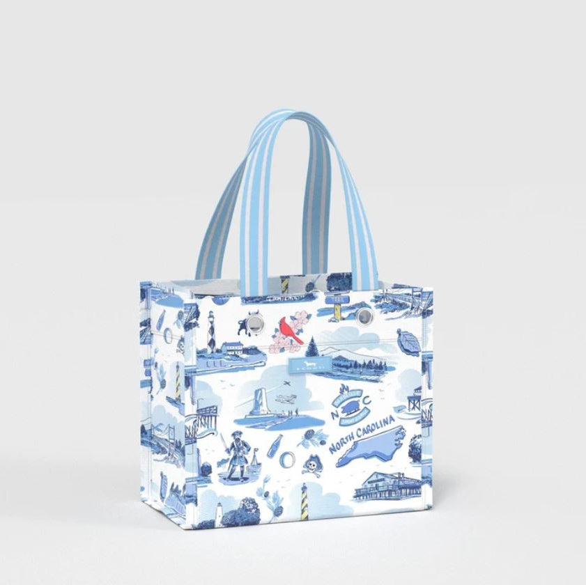 A reusable tote bag featuring a blue and white North Carolina-themed toile-style print with illustrations of landmarks, lighthouses, and the text 'North Carolina', complete with two light blue and white striped handles, set against a plain light gray background.