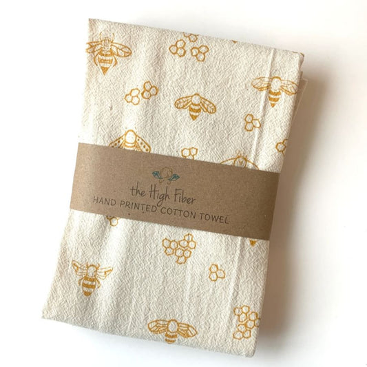 Folded hand-printed cotton towel with bee pattern and 'the High Fiber' label on a white background
